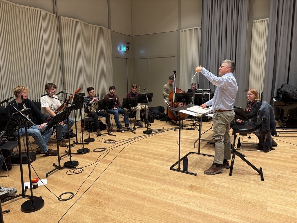 Student musicians in the Recital Hall, with Professor Traill conducting, and Anna Clyne and Jody Elff at desks in front of them. 